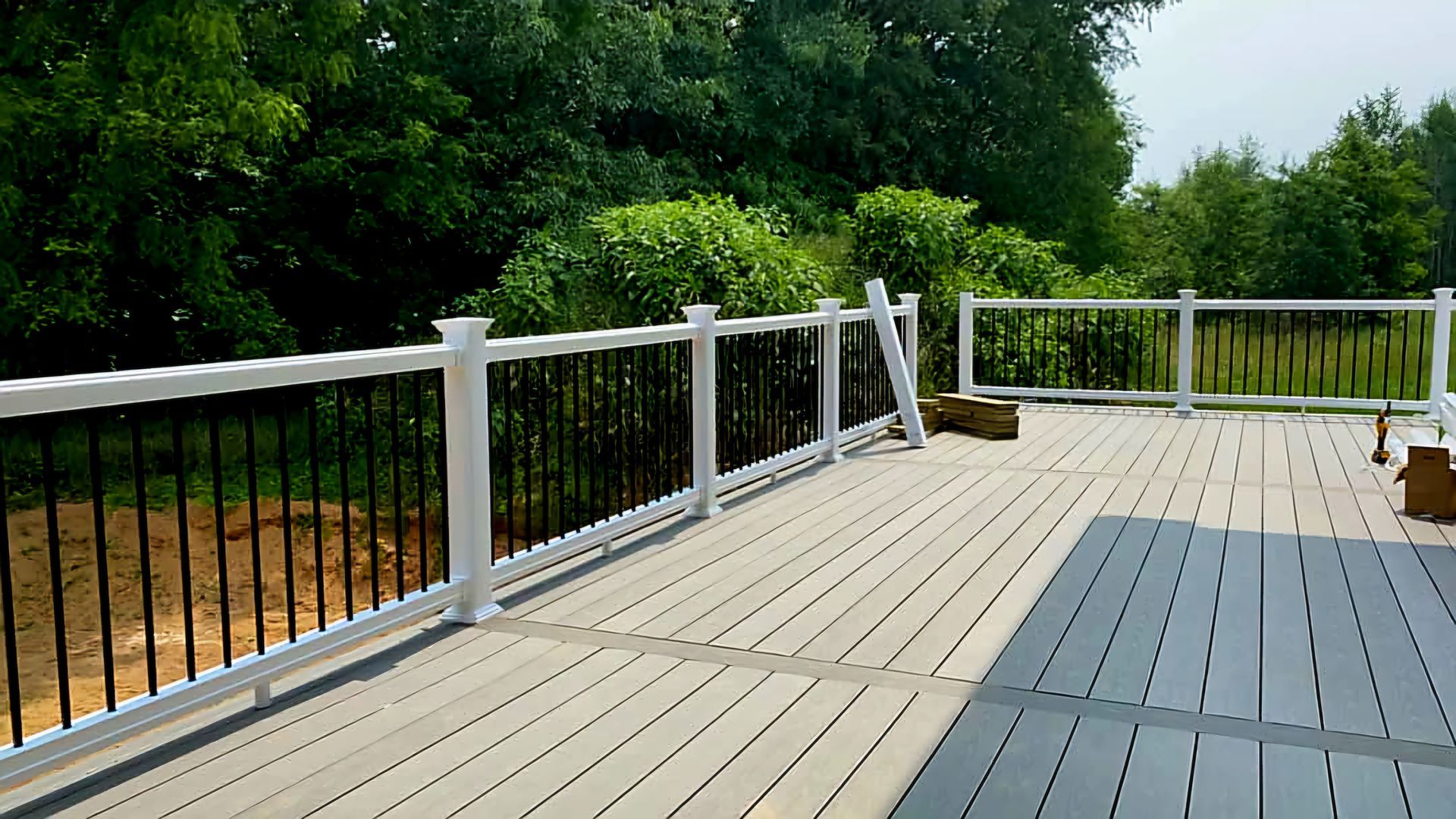 Empty gray deck with white railing overlooking trees and a grassy yard