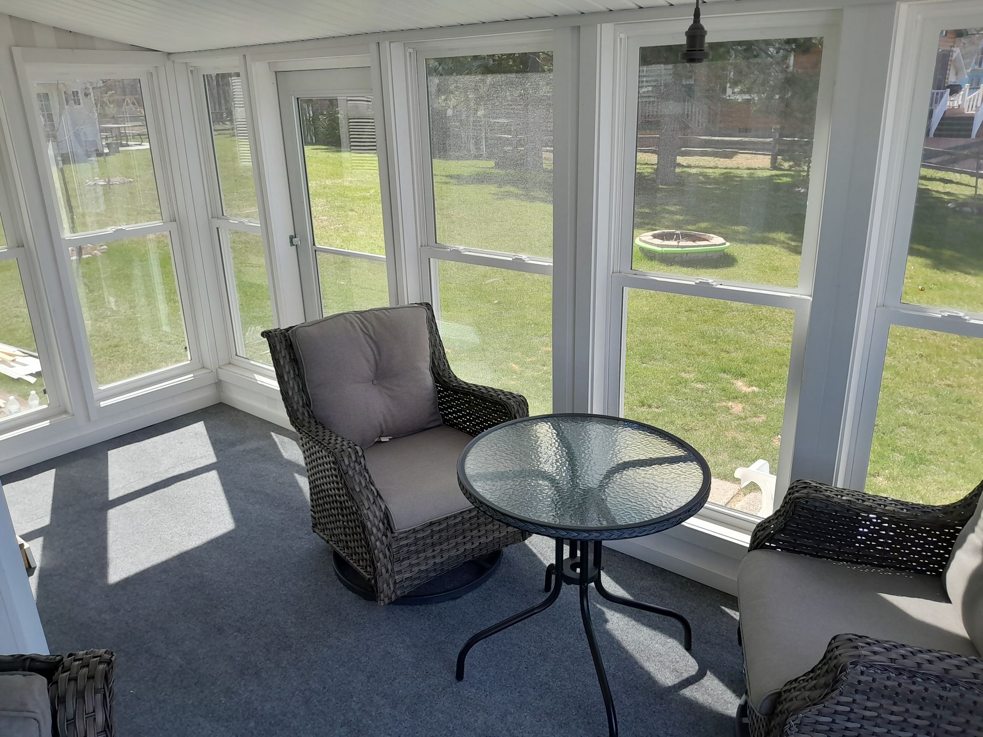 Sunroom with wicker chairs and a glass table beside large windows overlooking a green yard