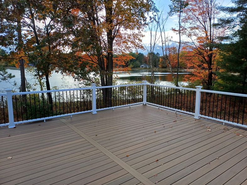 Wooden deck overlooking a lake, with autumn trees and a white railing under a cloudy sky