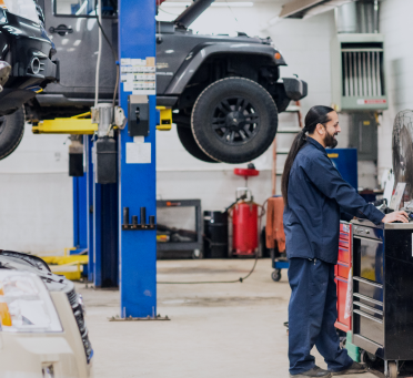 Mechanic working in an auto repair shop beside a vehicle lifted on a blue hydraulic hoist | Mears Automotive