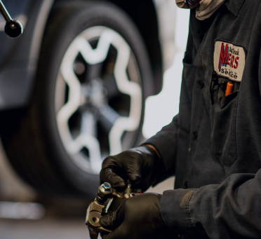 Mechanic in dark uniform and gloves working on a car wheel in a garage | Mears Automotive