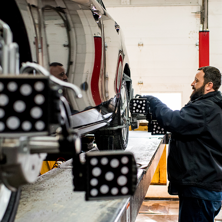 Worker inspecting a shiny vehicle in a workshop, with reflective panels and equipment nearby | Mears Automotive