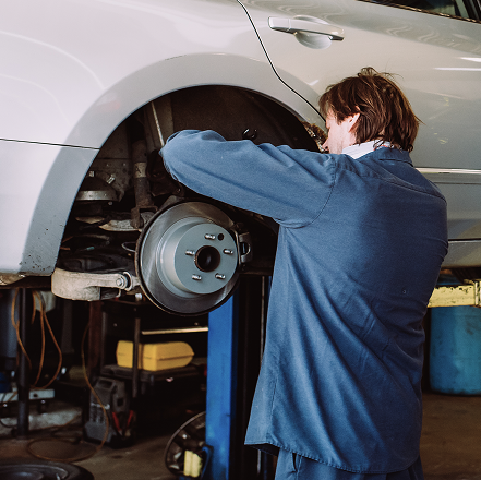 Mechanic working on a car’s exposed front wheel brake assembly in a garage | Mears Automotive
