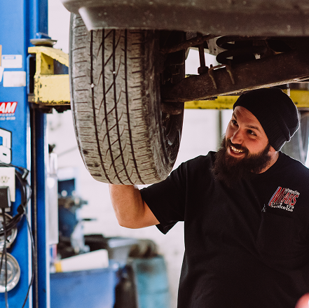 Mechanic inspecting a lifted car’s tire in an auto repair shop | Mears Automotive