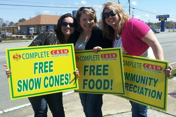 Three women holding signs offering free snow cones, free food, and community recreation outdoors