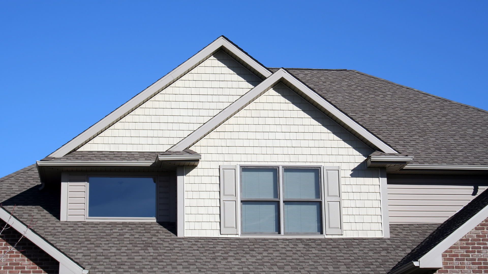 A house with a dark roof and dormer windows against a clear blue sky.