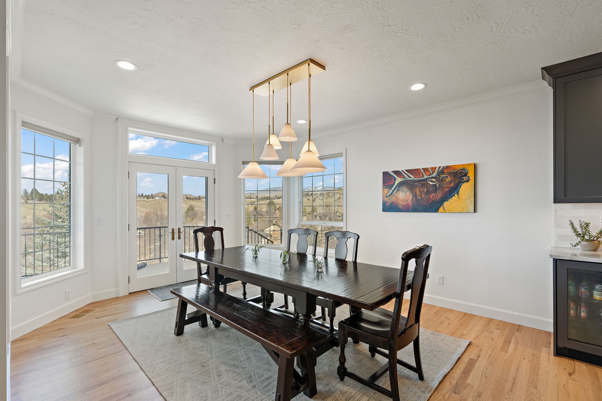 Dining room with dark wooden table, bench, and chairs. Light-colored walls, large windows, and pendant lights.