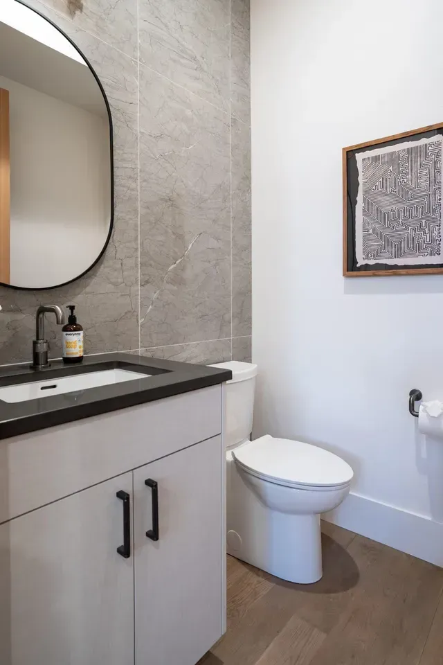 Double vanity bathroom with two round mirrors, sconces, and gray wooden cabinets.