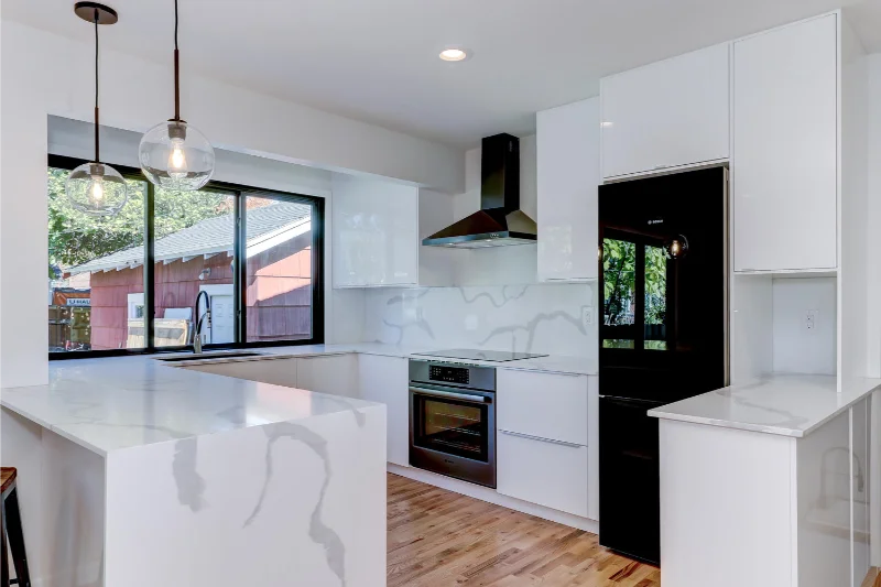 Modern white kitchen with black appliances and accents, including a range hood, fridge, and window frames.