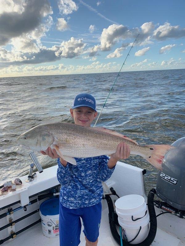Boy on boat holding a large redfish. Ocean backdrop, cloudy sky.