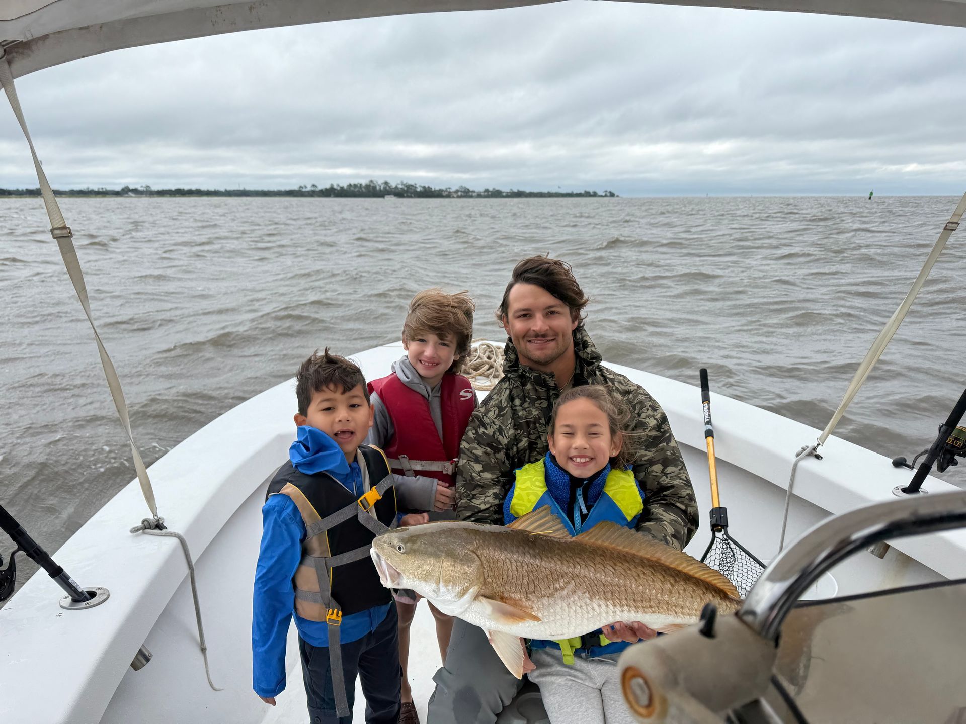 Family on a boat holding a large fish, cloudy sky over water.