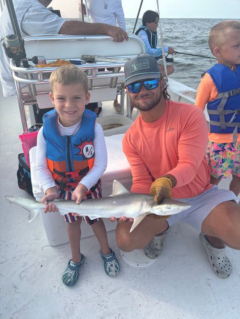 A man and a boy on a boat hold a small fish. The boy smiles, wearing a life vest.