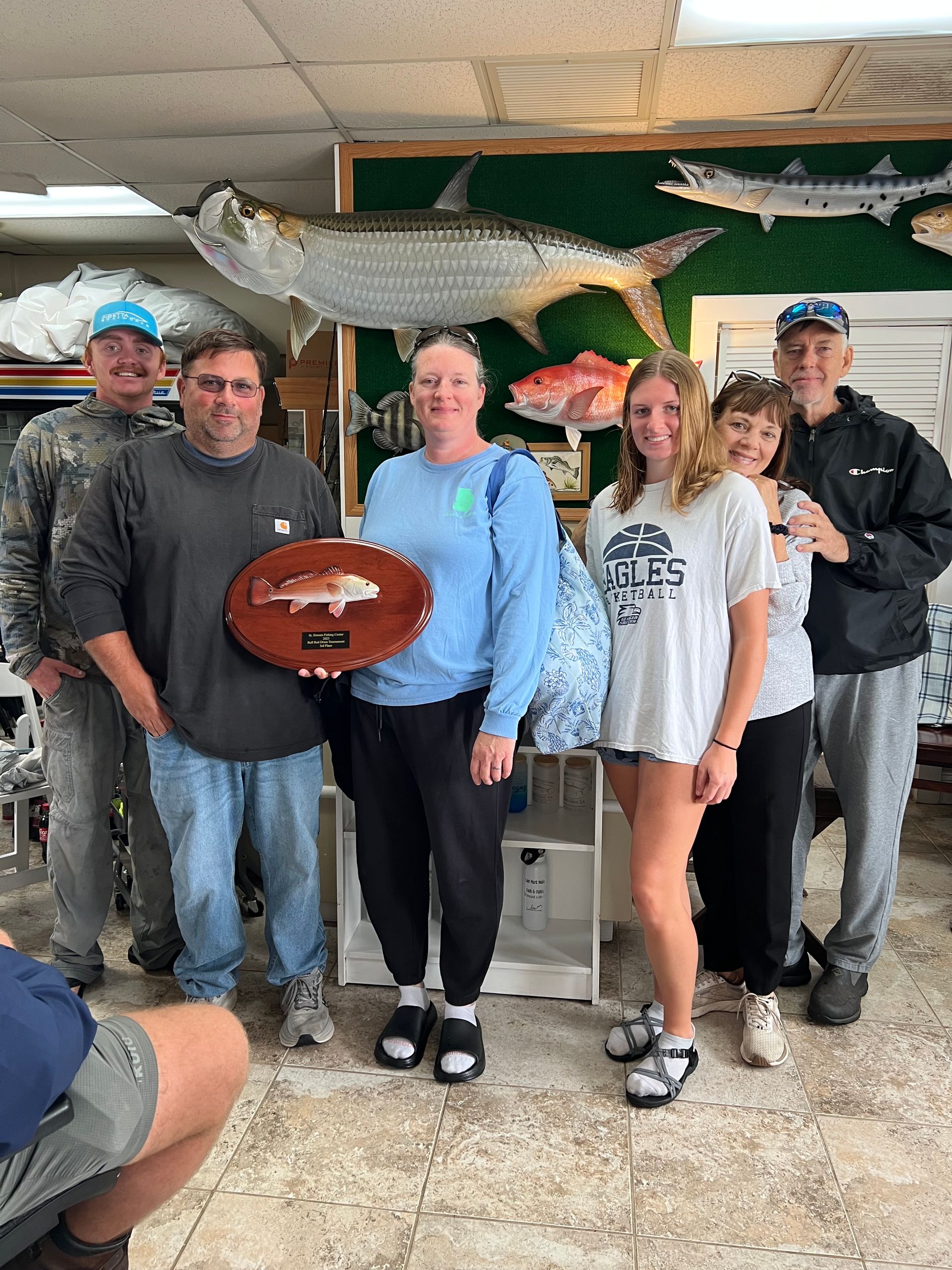 Group of people holding an award in a shop with fish decorations. Woman in blue holding trophy.