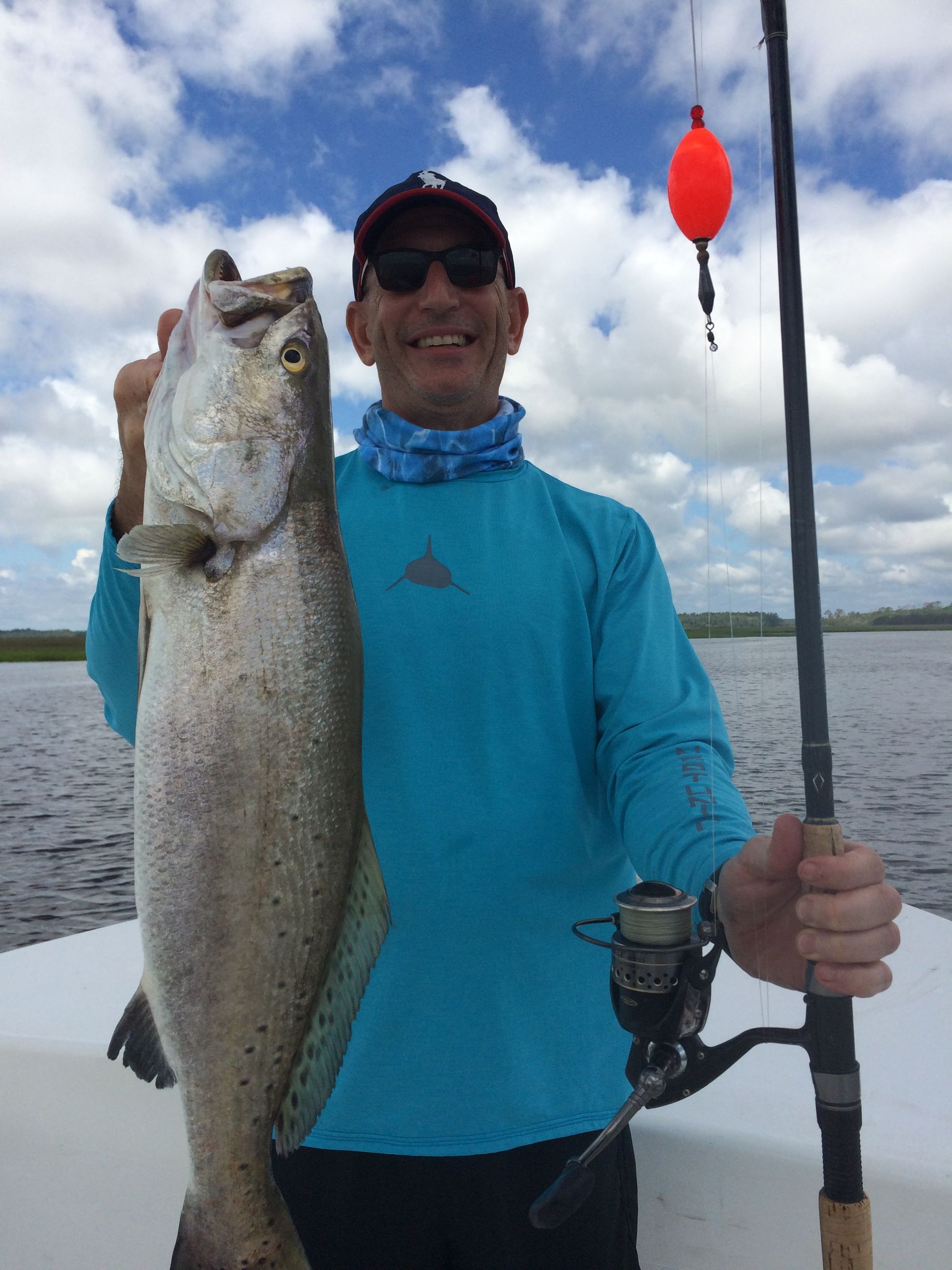 Man holding a large fish on a boat, smiling under a cloudy sky.
