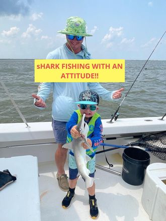 A man and child on a boat holding a fish. The boy wears sunglasses and a life vest, the man wears a hat.