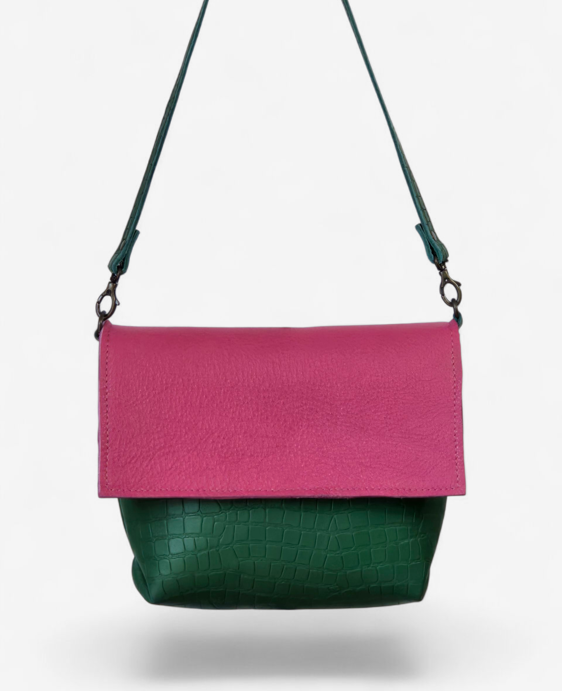 Een crossbodytas met een roze suède klep en een donkergroene body van leer met krokodillenprint, die afsteekt tegen een witte achtergrond.