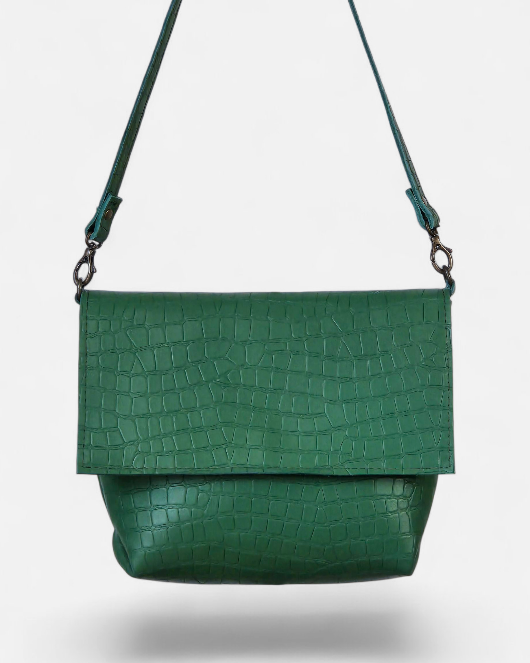 Een groene crossbodytas met een krokodillenprint en een vouwsluiting op een witte achtergrond.