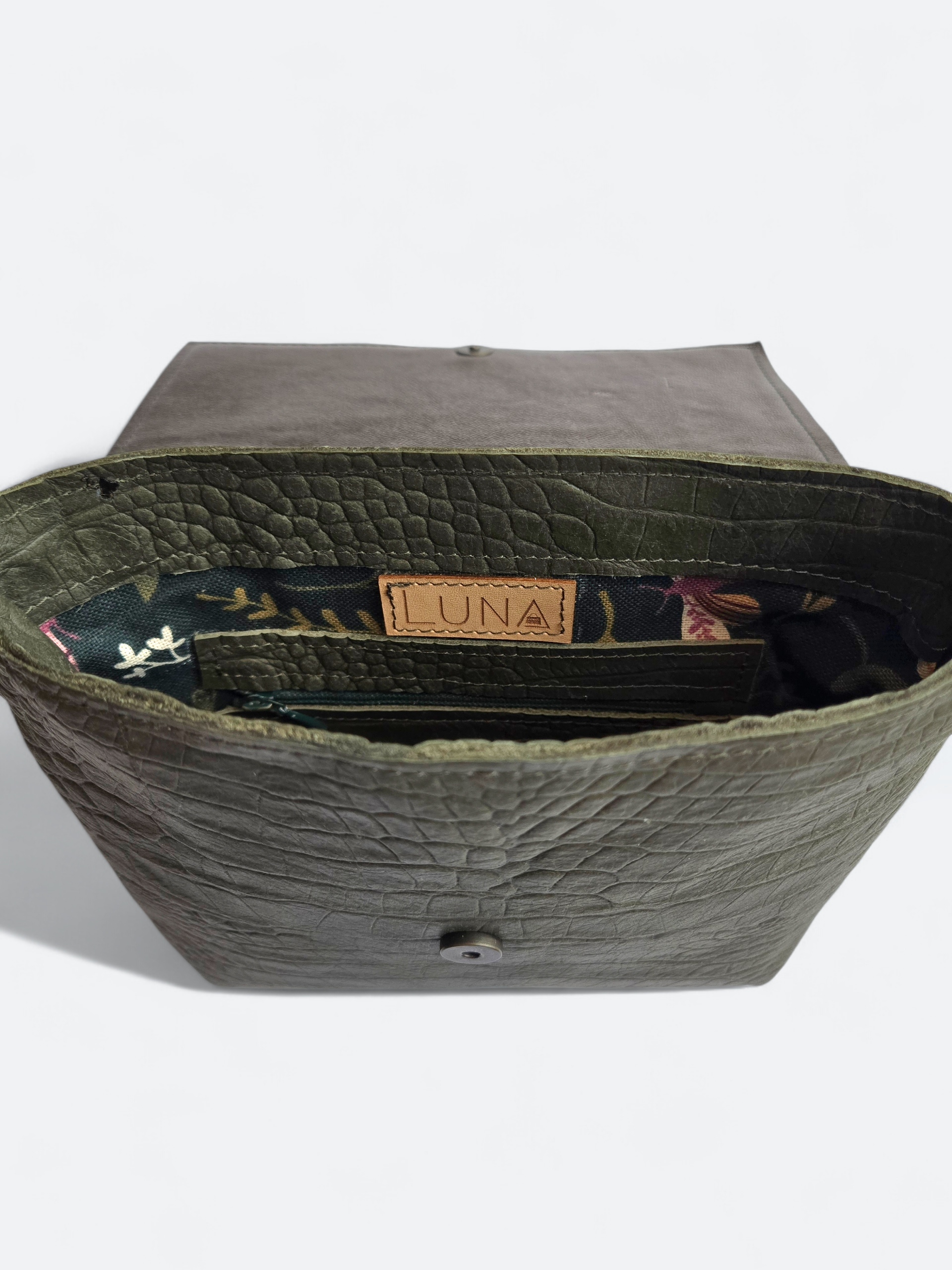 Een donkere, metallic bronzen, rechthoekige crossbodytas met klep en een smalle schouderband op een witte achtergrond.
