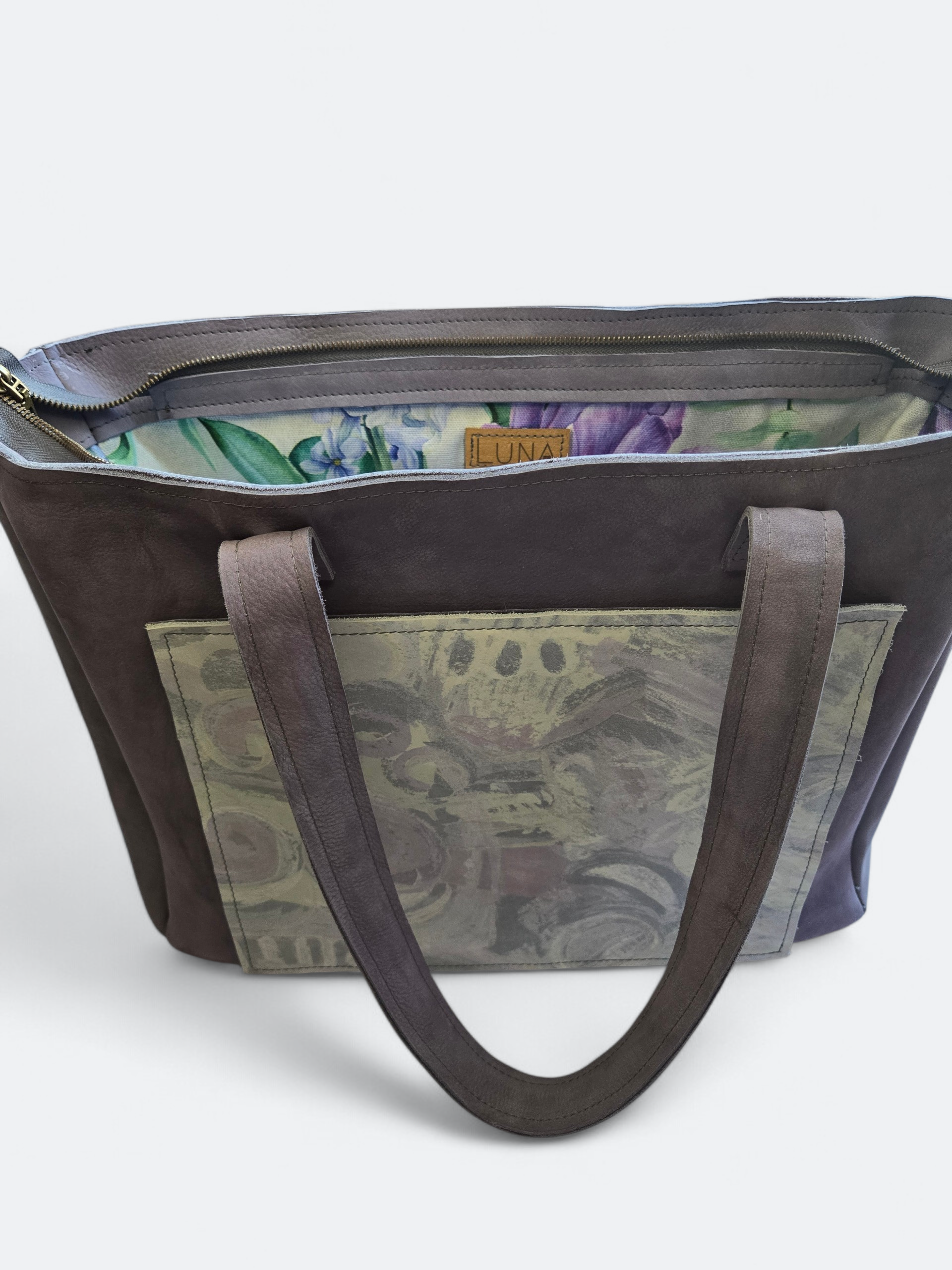 Een antracietgrijze suède shopper met een voorvak met patroon en een bloemenprint aan de binnenkant, van bovenaf gezien.