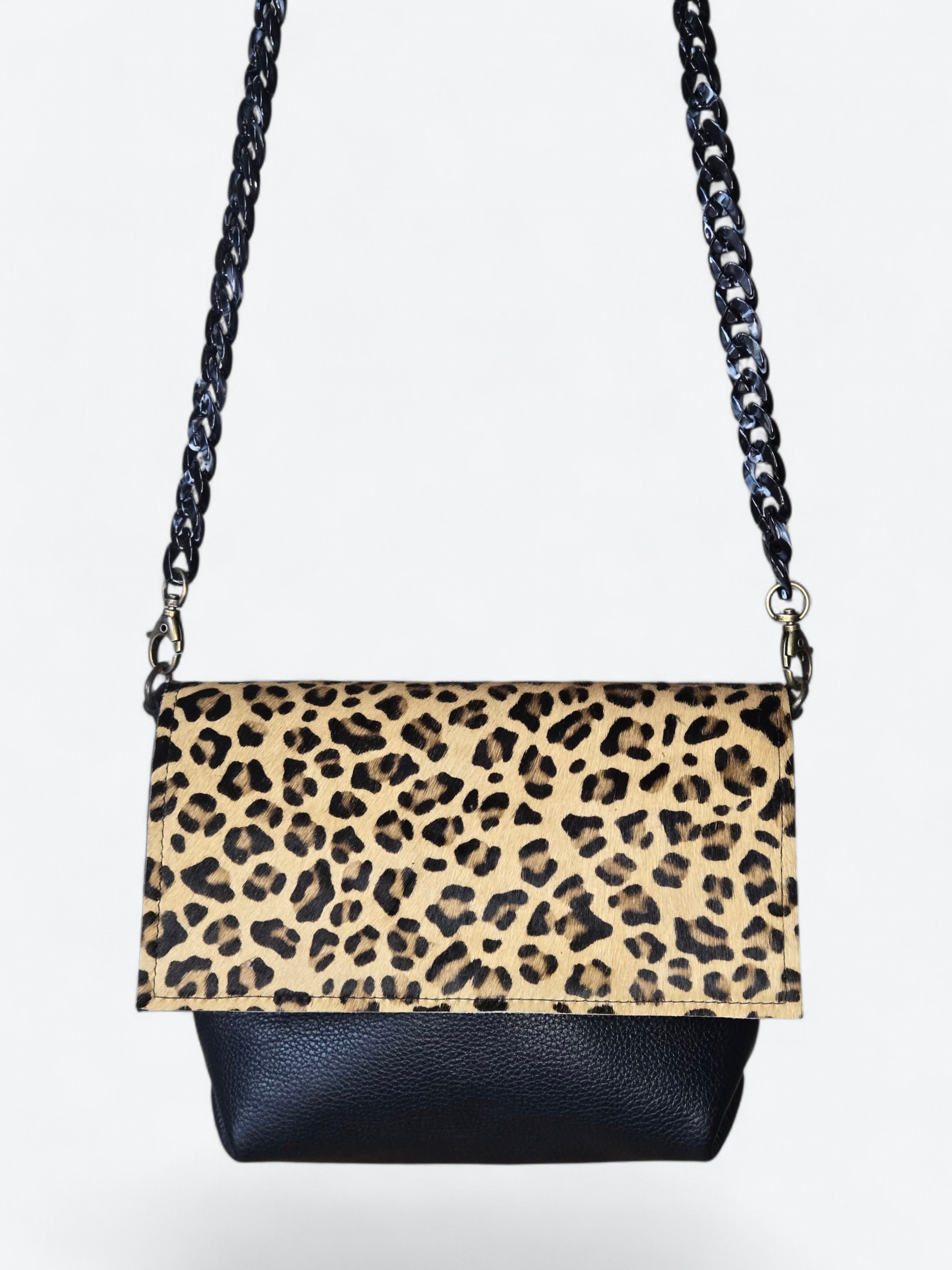 Crossbodytas met klep en luipaardprint, zwarte kettingriem en effen achtergrond.