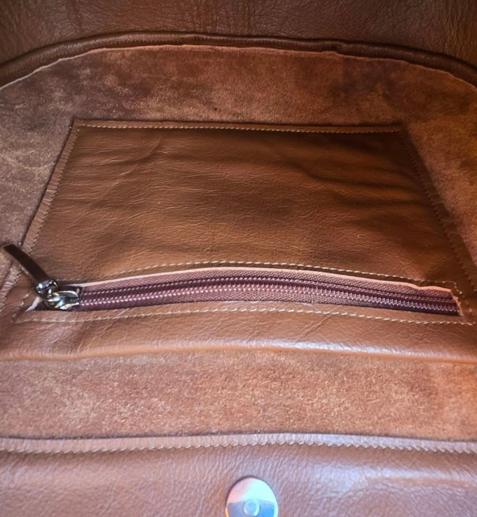 Een binnenaanzicht van een bruine leren tas met een ritsvak en een magnetische sluiting aan de onderkant.