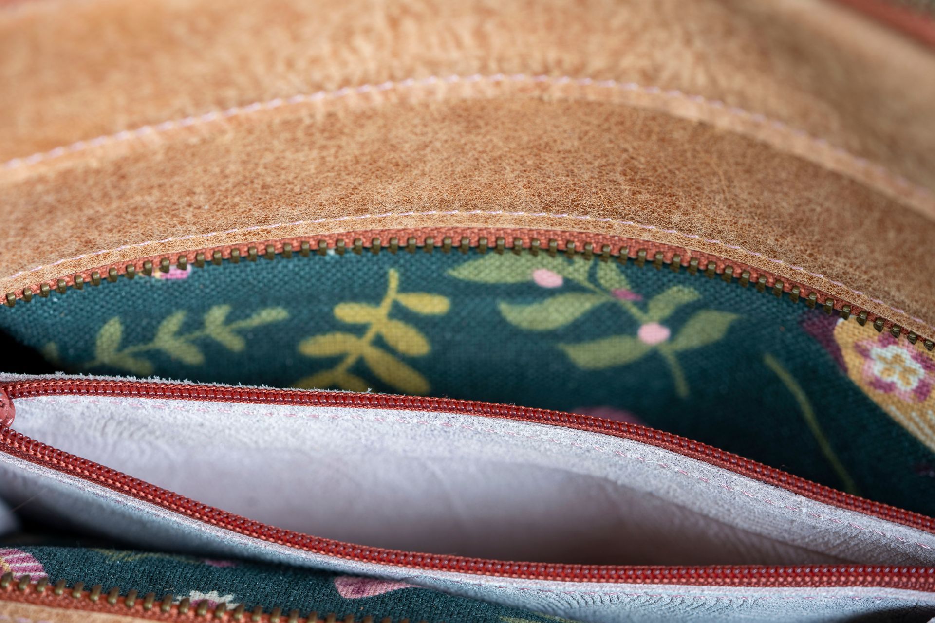 Een close-up van de binnenkant van een leren tas, met een groene voering van bloemenstof en een lichtgekleurd vakje met ritssluiting.