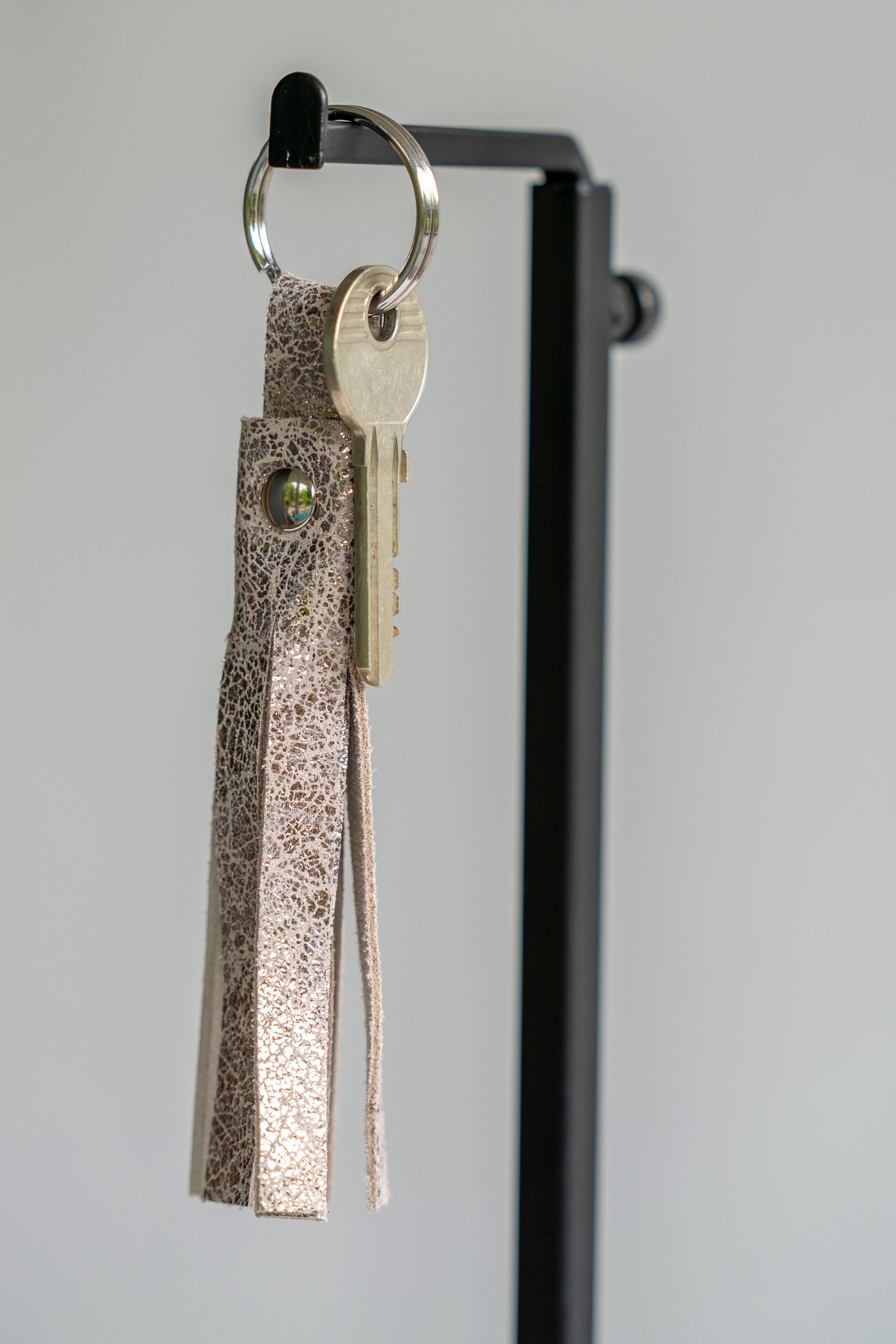 Vier leren sleutelhangers met kwastjes in de kleuren blauw, roze, rood en metallic zilver, verticaal gerangschikt op een witte ondergrond.