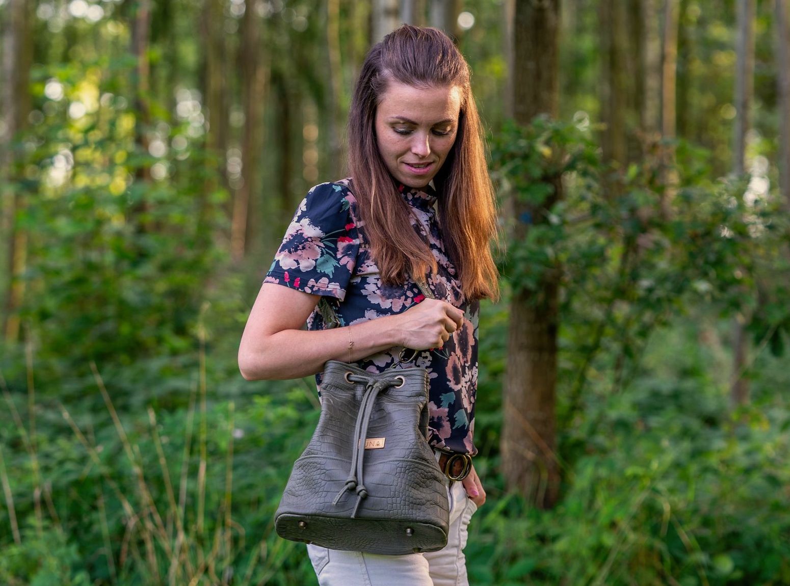 Een olijfgroene leren tas met trekkoord en een gestructureerde afwerking staat op een houten ondergrond in een tuin.