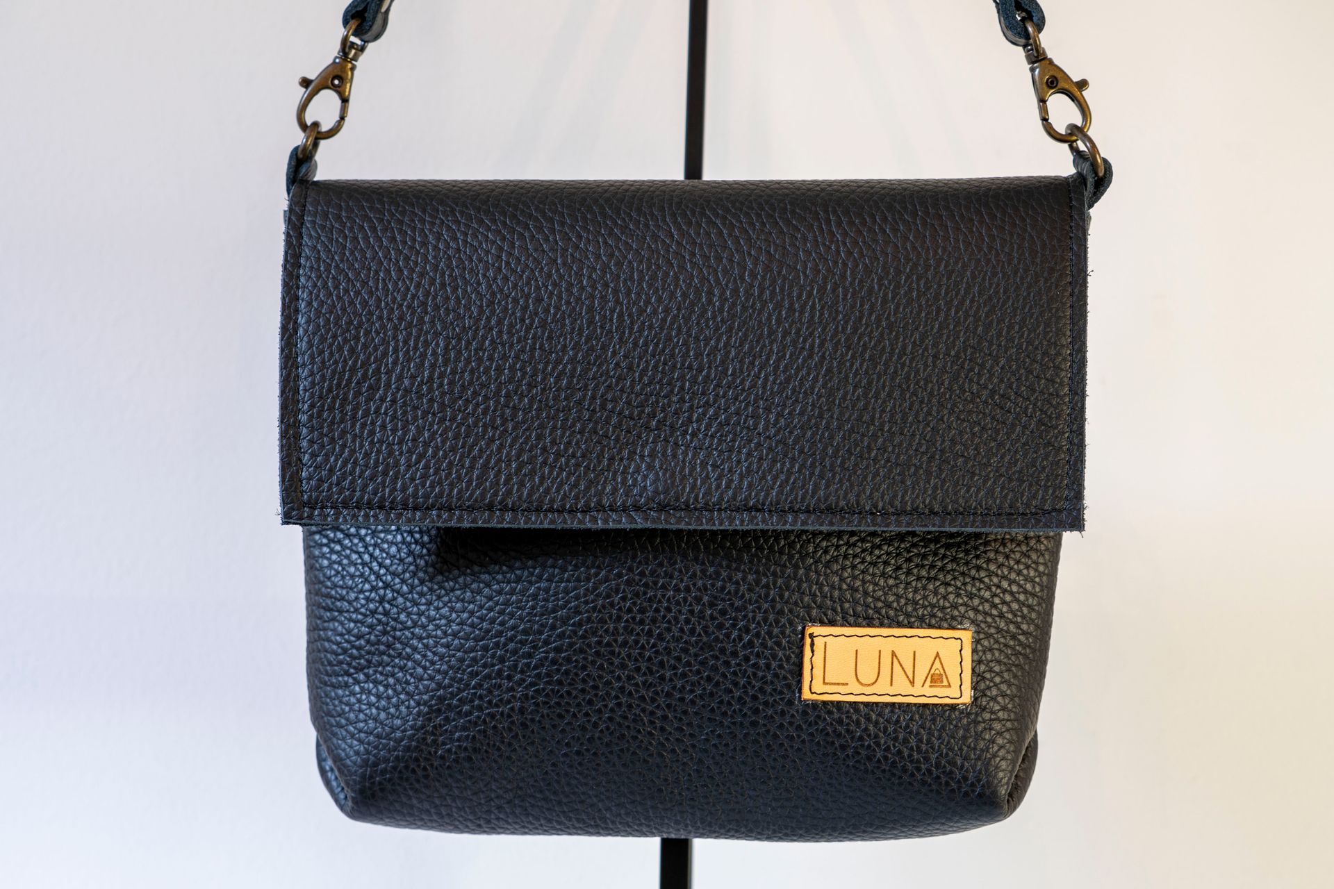 Een zwarte, gestructureerde leren crossbodytas met een omgeslagen klep en een gouden
