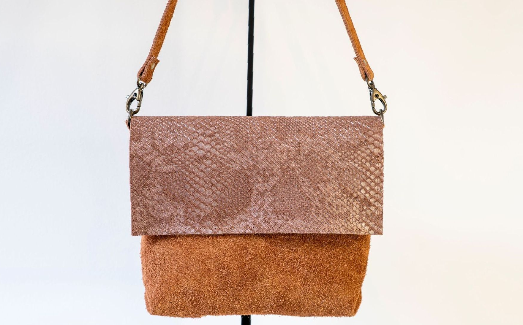 Een tweekleurige crossbodytas met een gestructureerde metallic koperkleurige overslagklep en een zachte, pluizige bruine leren buitenkant.