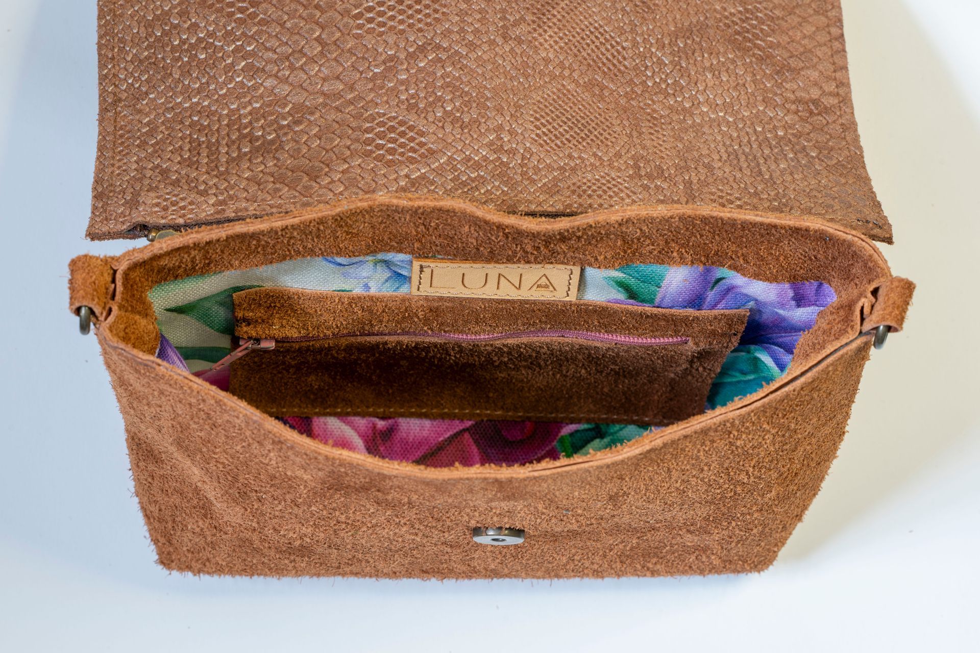 Een tweekleurige crossbodytas met een gestructureerde metallic koperkleurige overslagklep en een zachte, pluizige bruine leren buitenkant.
