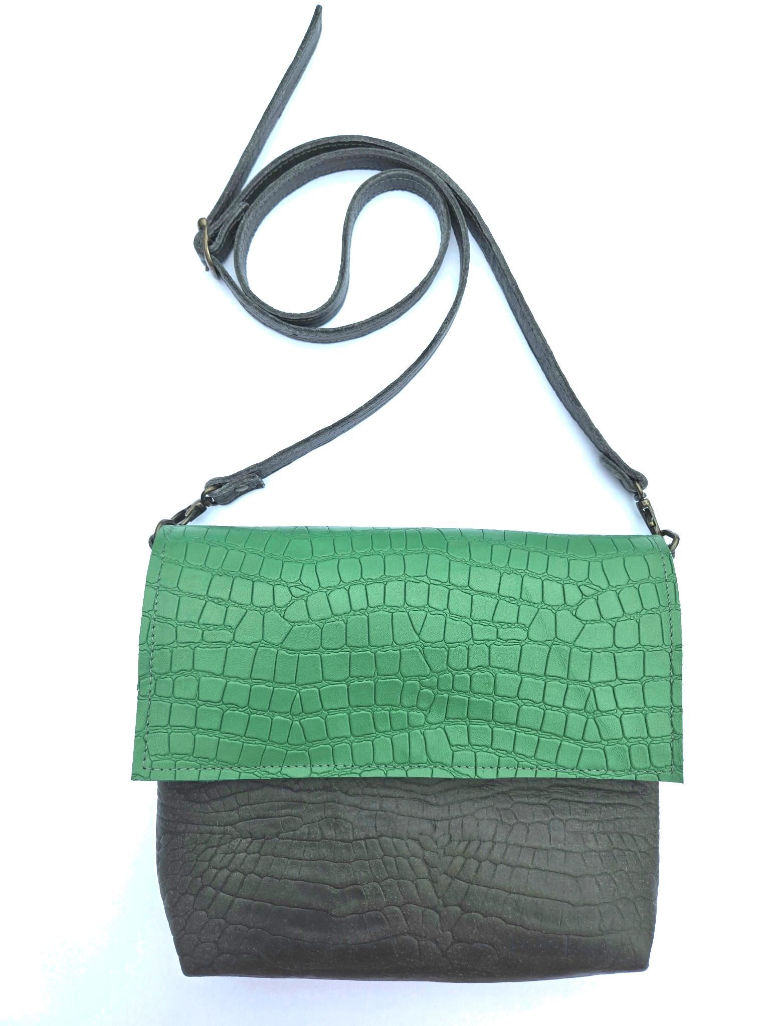 Een tweekleurige crossbodytas met een groene, gestructureerde klep en een donkerbruin hoofdgedeelte, die aan een dunne schouderband hangt.