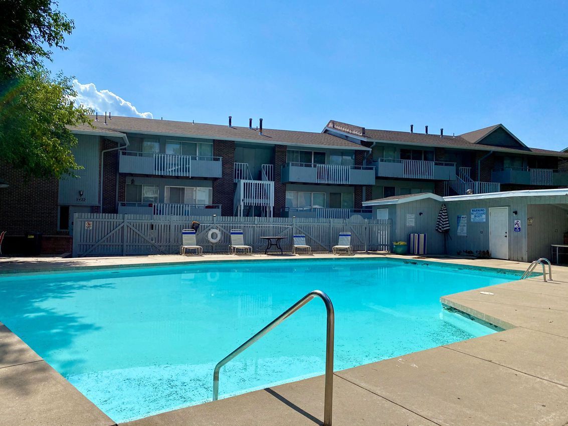 Pool in front of a two-story apartment building with balconies on a sunny day.