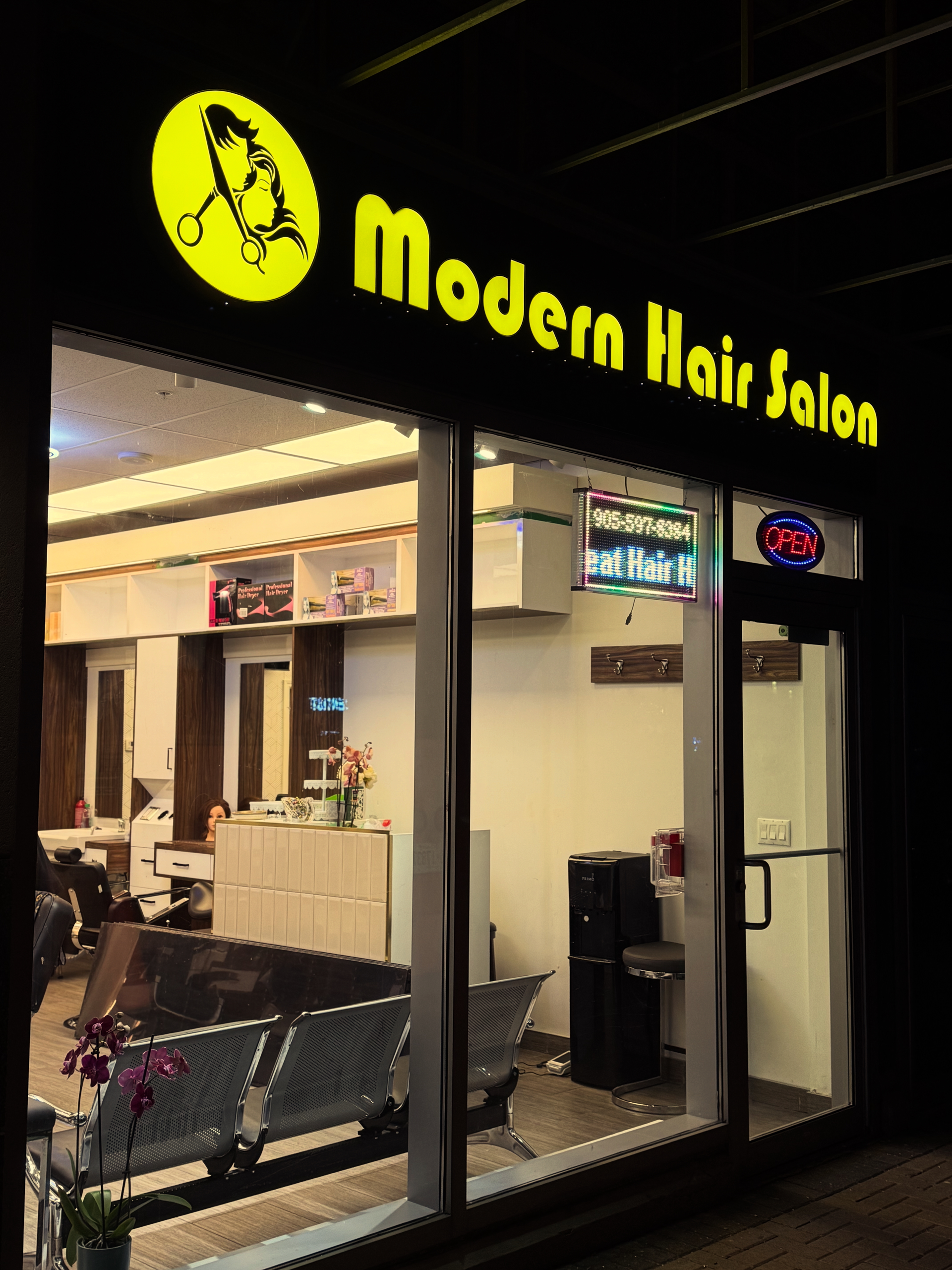 Modern Hair Salon storefront with yellow sign illuminated at night. Interior visible.
