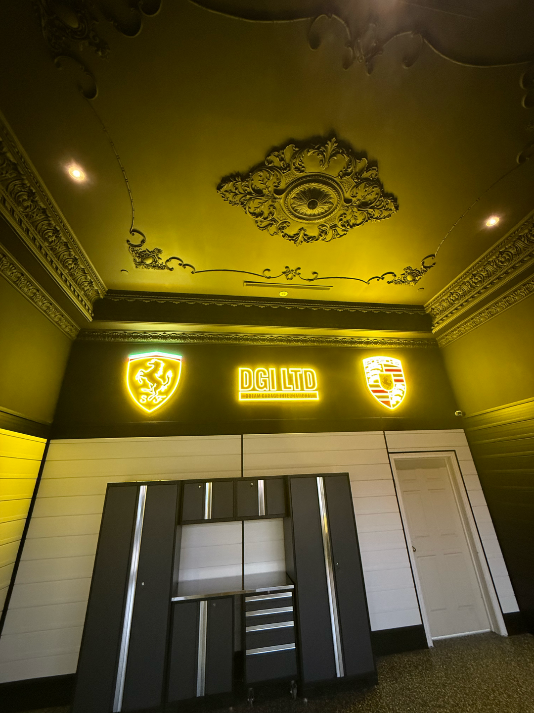 Garage interior with black cabinets, yellow neon logos, and ornate ceiling details.