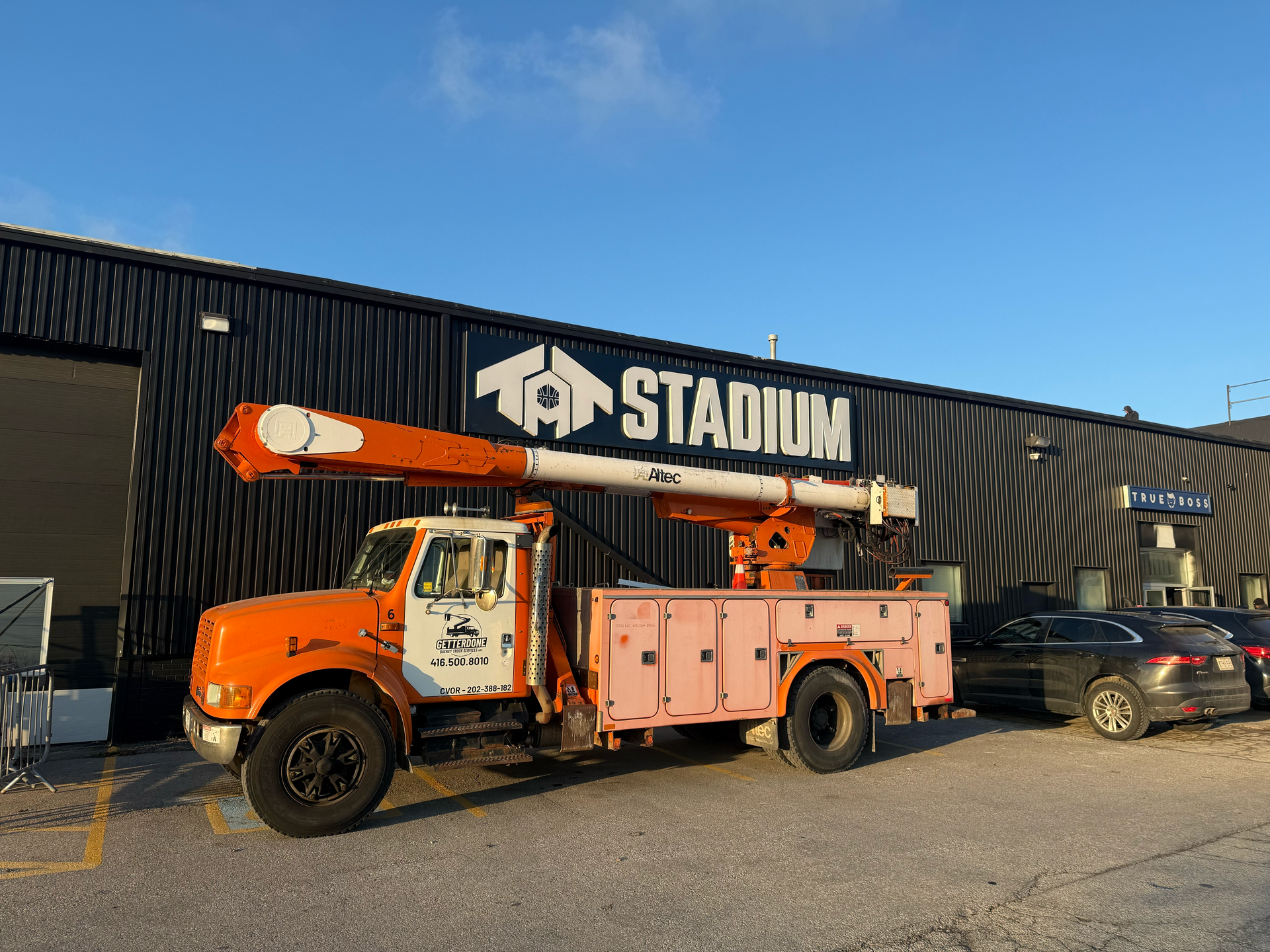 Orange utility truck with extended boom arm parked outside a building with 