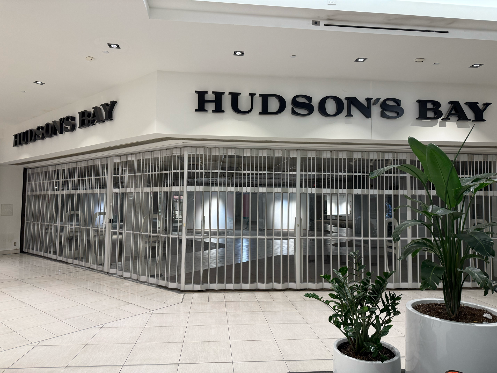Closed Hudson's Bay store in a mall, with security gates. Plants in planters.