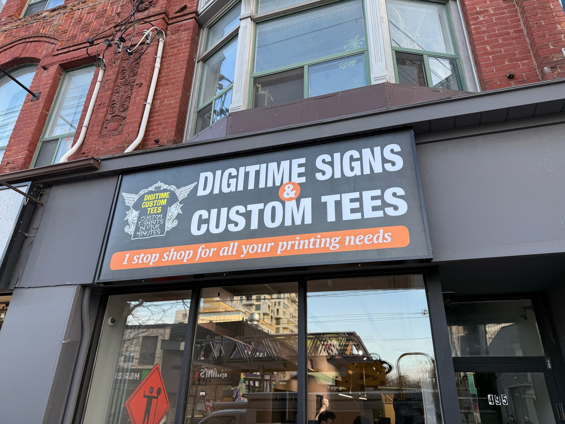 Digitime Signs & Custom Tees storefront with sign and window display on a brick building.