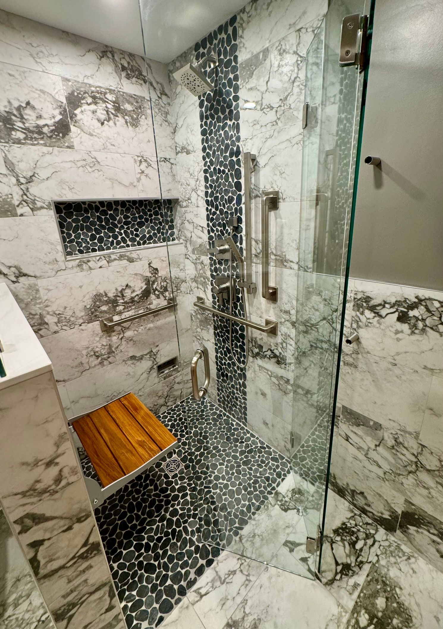 Modern shower with marble walls, glass enclosure, bench, and mosaic tile floor
