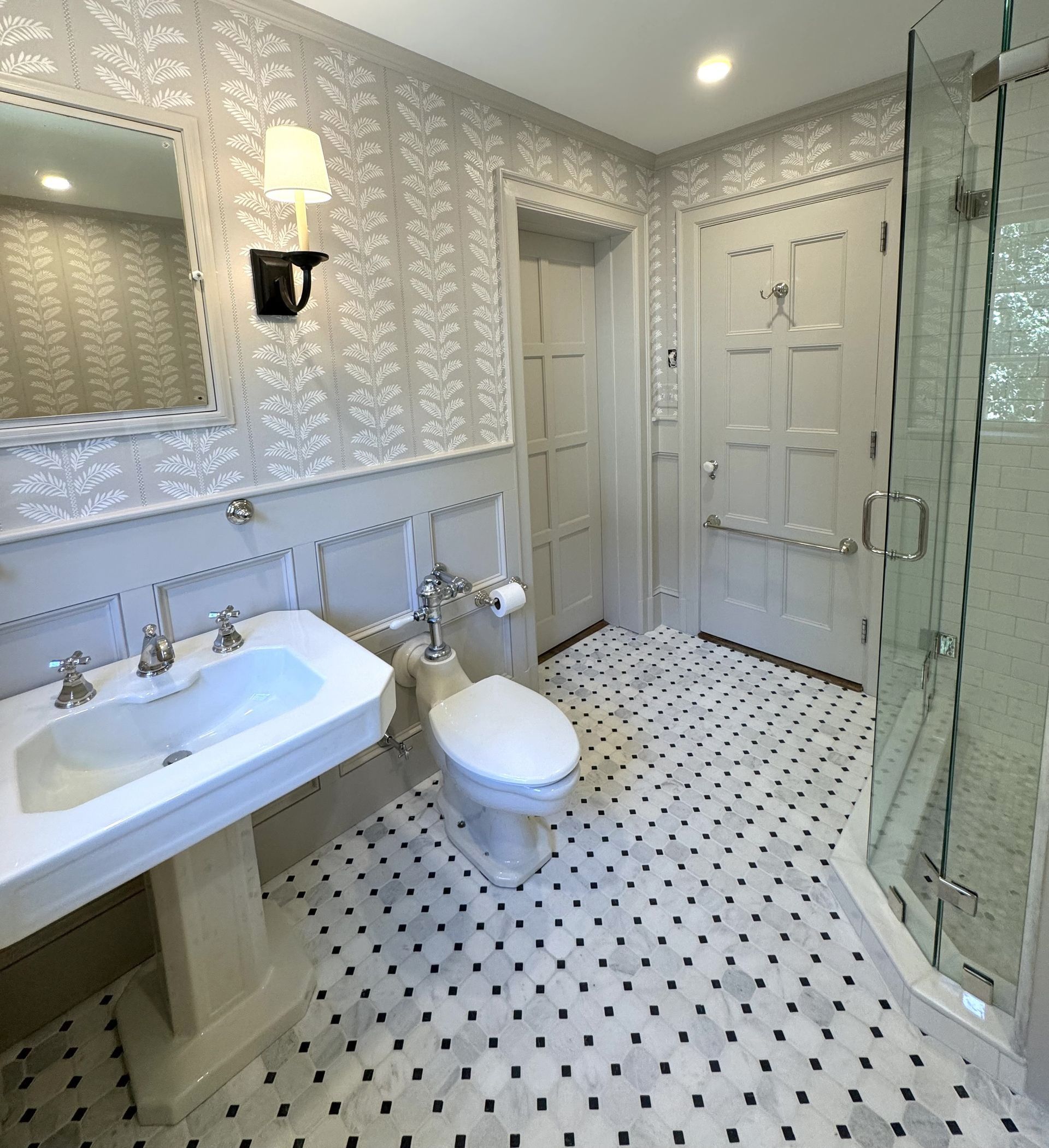 Bright white bathroom with patterned tile, vanity, toilet, and glass shower enclosure