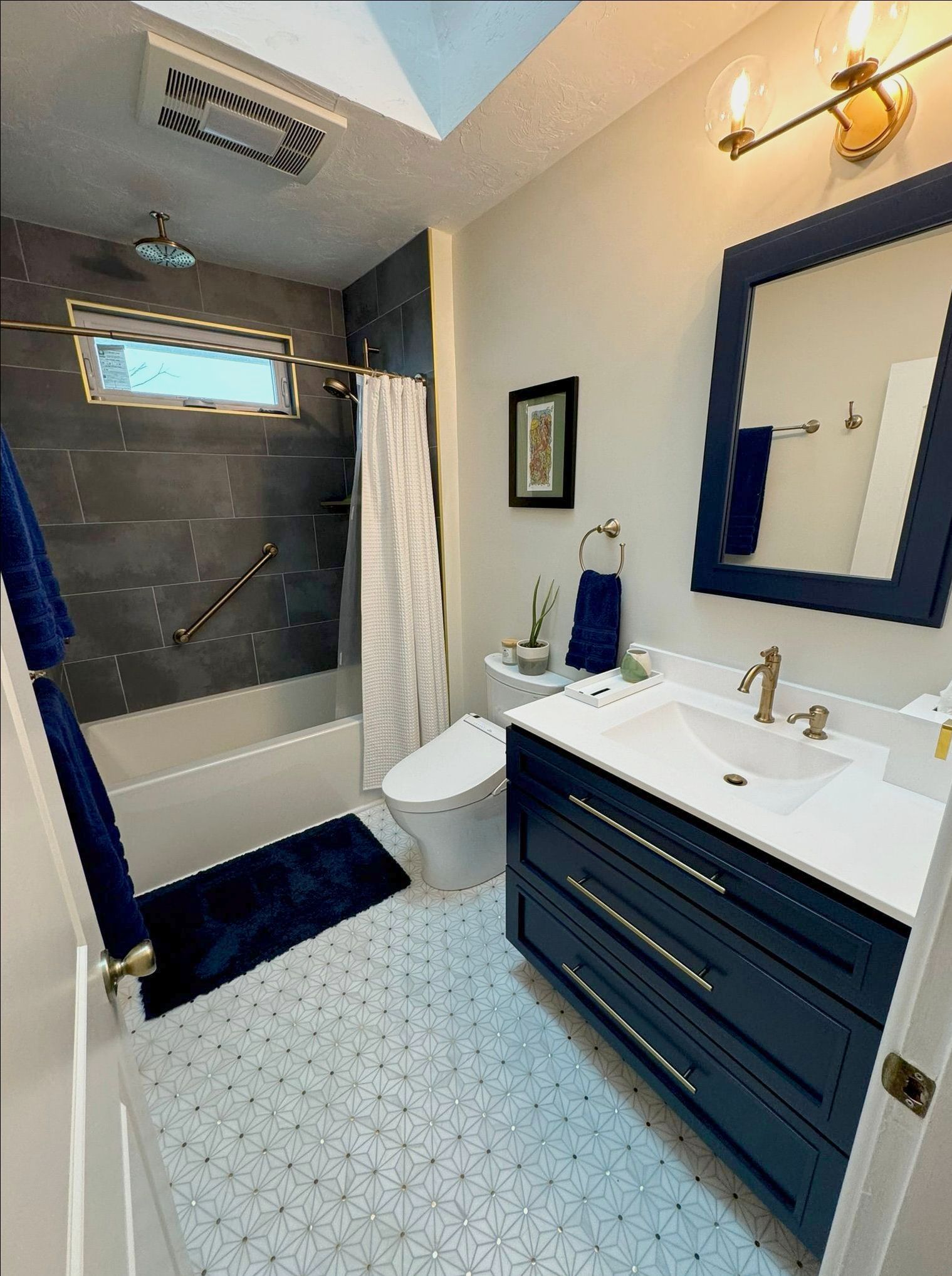 Modern bathroom with navy vanity, white sink, mirror, and tiled tub shower.
