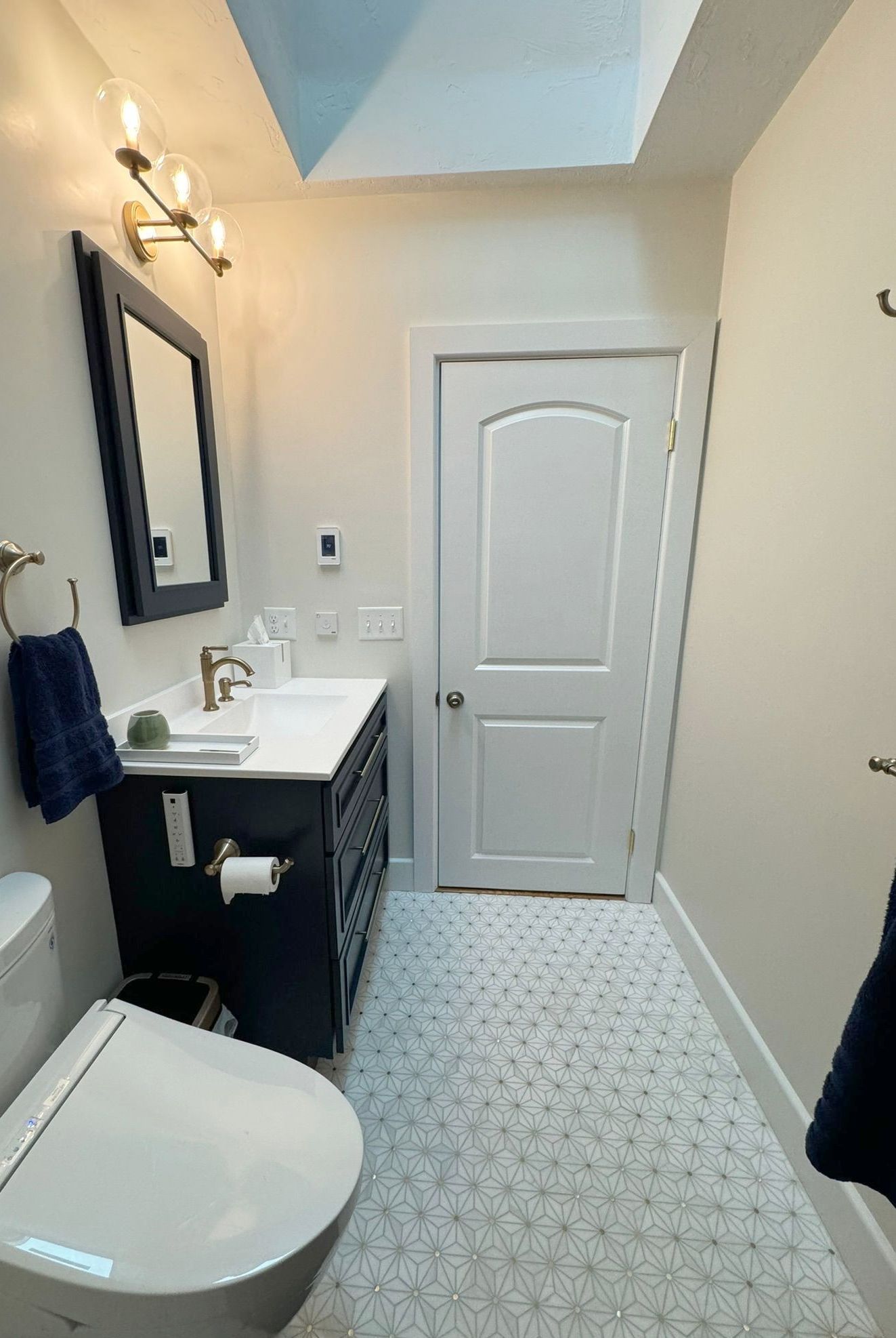 Small bathroom with vanity, sink, mirror, toilet, and patterned floor tile under a skylight.