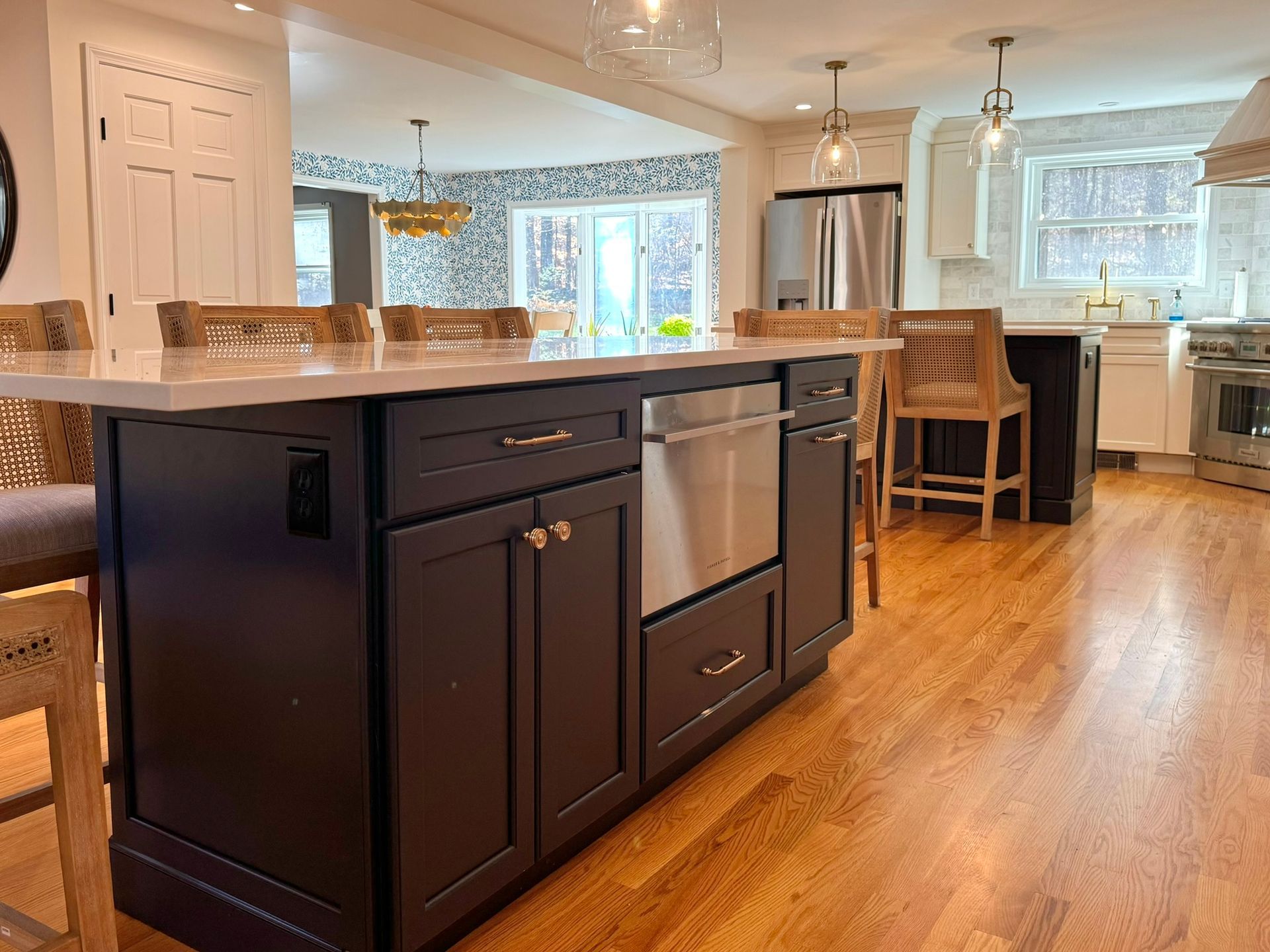 Bright kitchen with dark island, white countertops, hardwood floors, and dining area by large windows