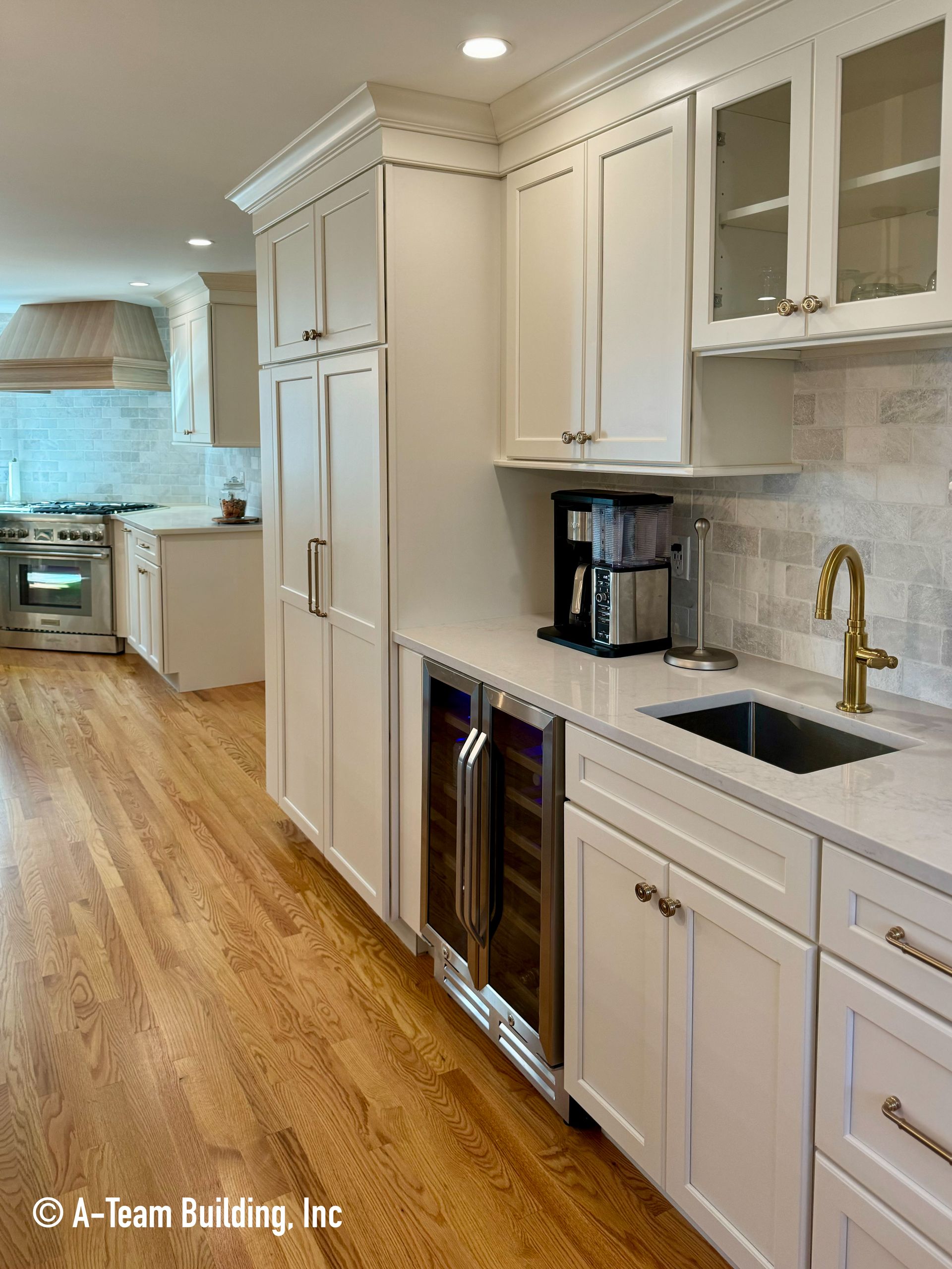 Bright white kitchen with long cabinets, wood floors, stainless appliances, and black coffee maker on the counter