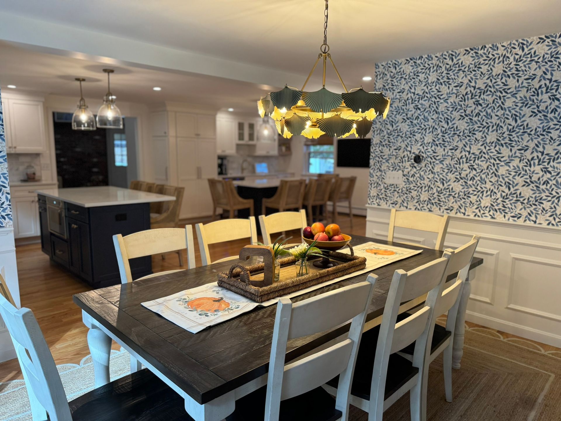 Dining room with a set table, dark wood island, and blue floral wallpaper in a bright open kitchen.
