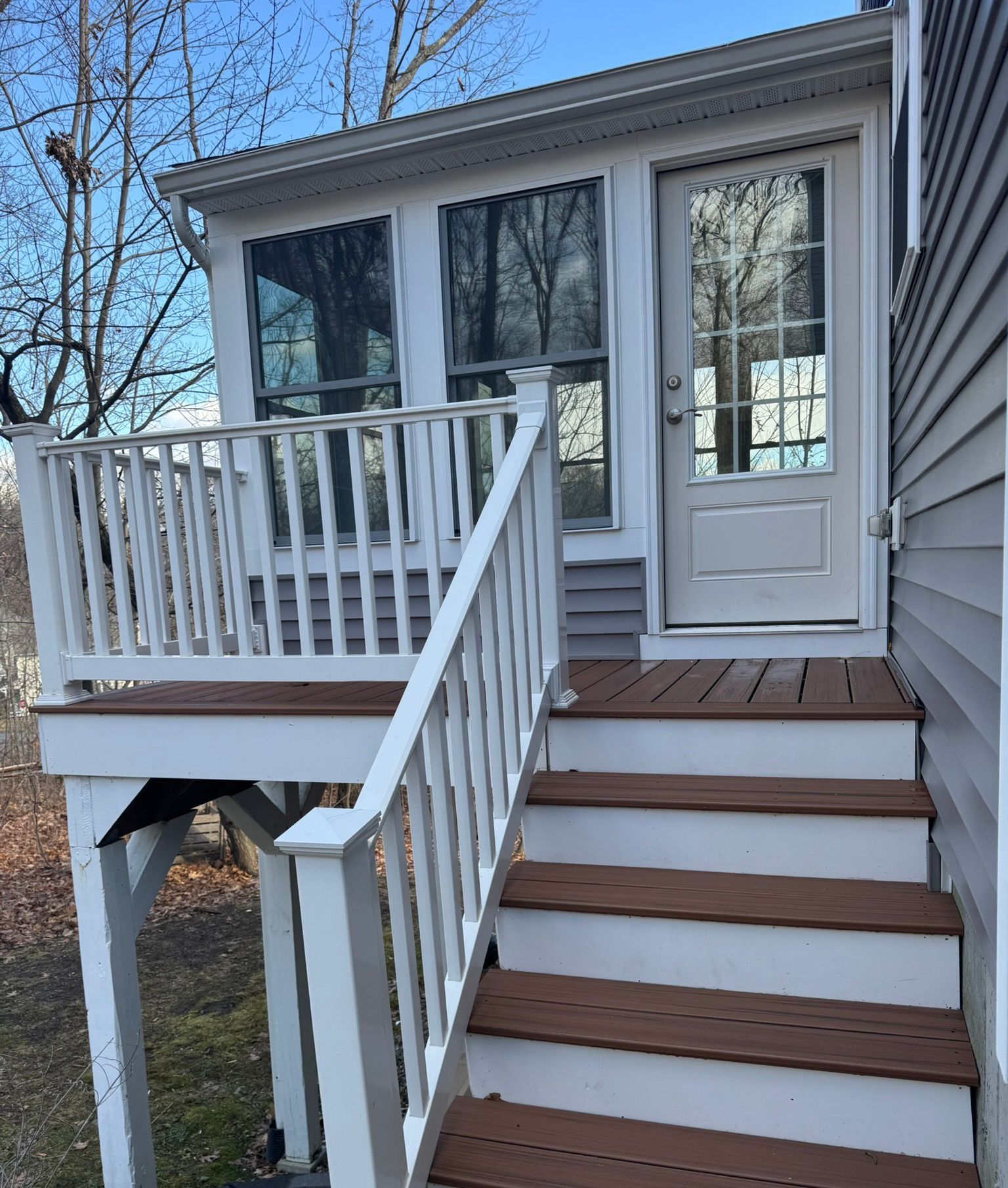 Front porch with white railings, brown steps, and a white door on a small house.