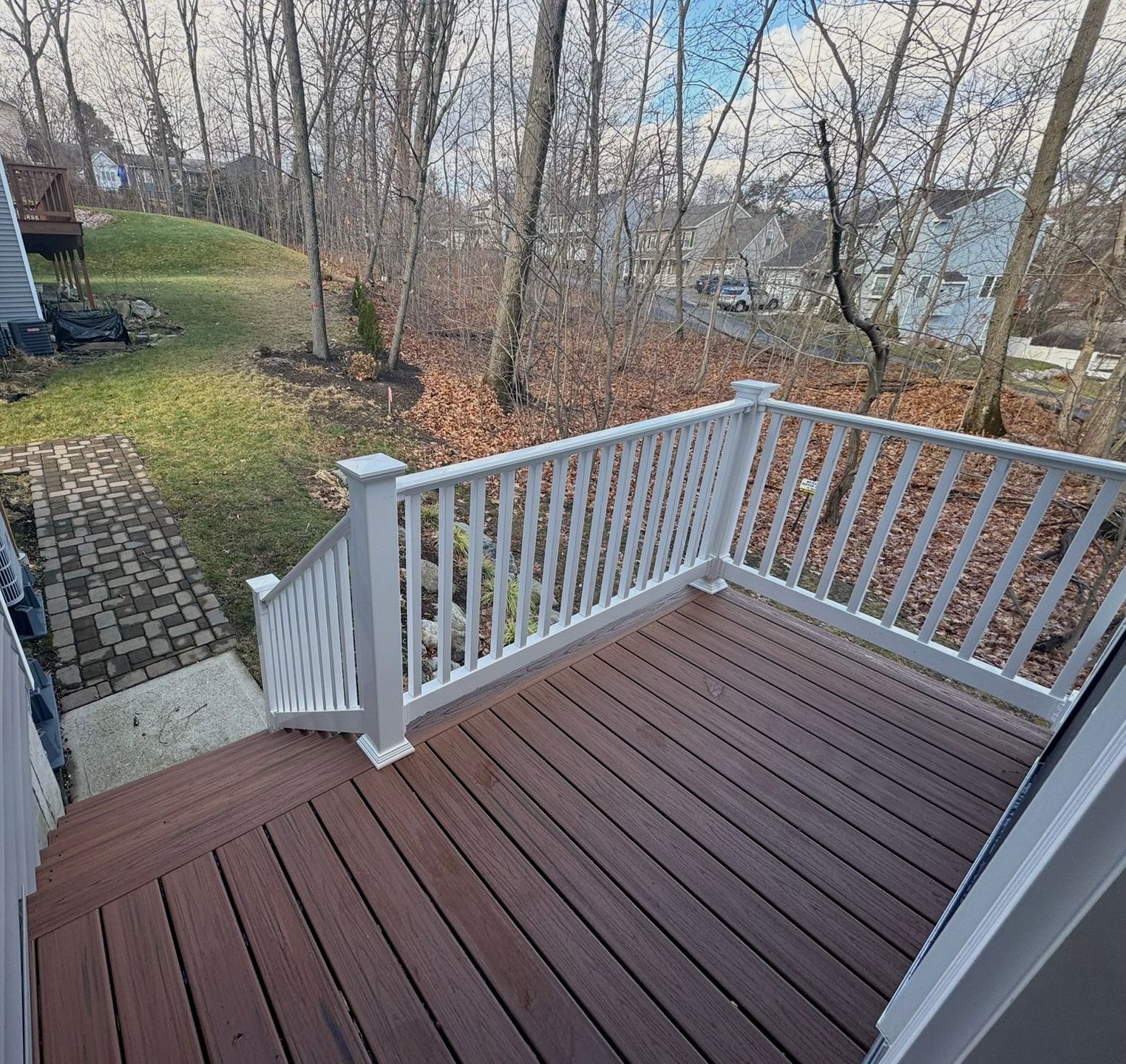 Back deck with brown flooring and white railings overlooking leafless trees and a yard