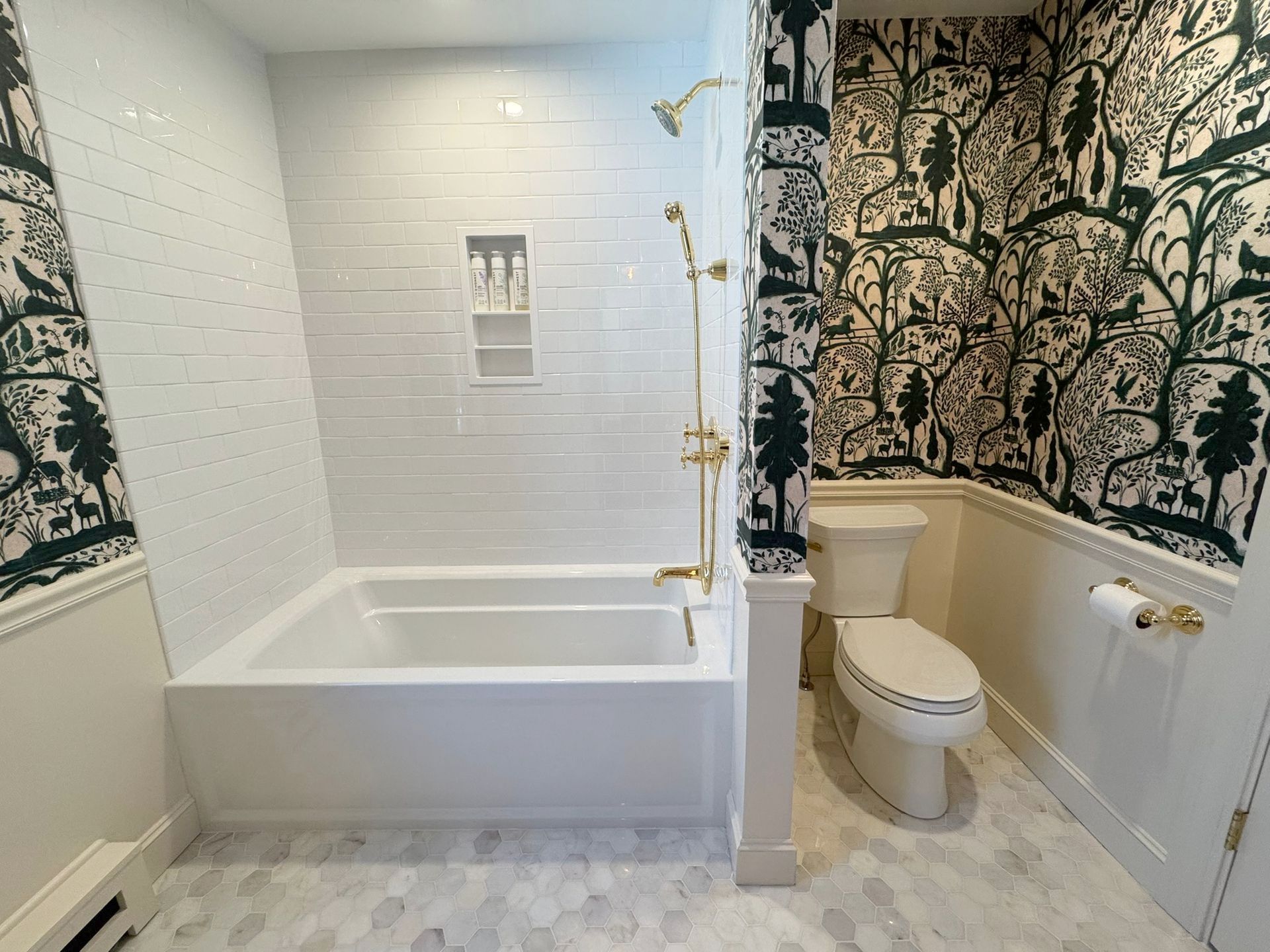 Bathroom with white tub, toilet, and patterned wallpaper, featuring gold fixtures and dark trim.