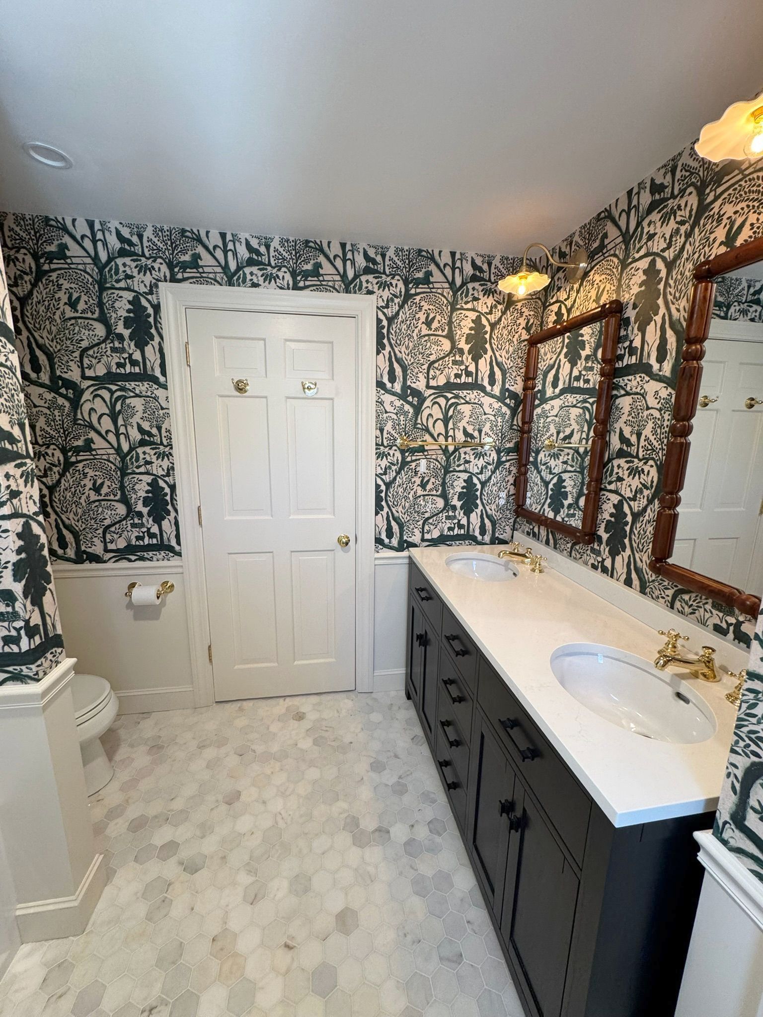 Bathroom with black-and-white floral wallpaper, white door, marble vanity, and mirror.