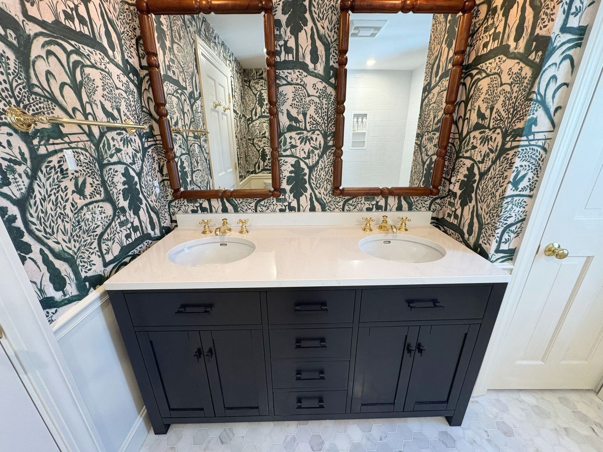 Double vanity bathroom sink with dark cabinets, white countertop, and patterned wallpaper with mirrors